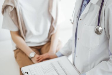Doktor ve hasta klinikte. Bir yandan dostane bir doktor genç bir kadını muayene ederken diğer yandan tıbbi kayıtlarla dolu bir pano tutuyor. Tıp konsepti.