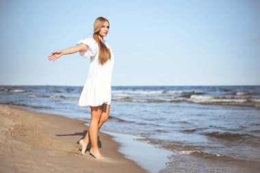 Mutlu gülümseyen güzel kadın okyanus sahilinde kollarını açmış yürüyor..