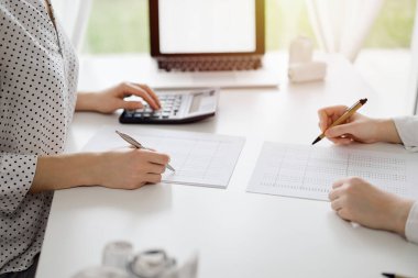 Hesap makinesi ve dizüstü bilgisayar kullanan iki muhasebeci vergileri ve gelir dengesini hesaplamak için beklerken makbuzlar da hesaplanmayı bekliyor. İş denetimi ve vergi kavramları.