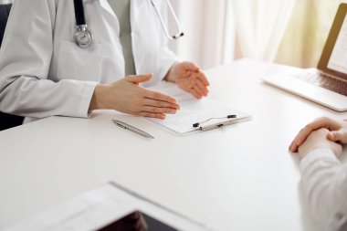 Doktor ve hasta klinikteki beyaz masada oturup bir şeyler tartışıyorlar. Kadın hekim bir kayıt formunu doldururken dinliyor. Tıp konsepti.