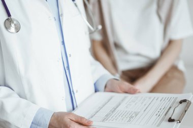 Doktor ve hasta mükemmel sağlık muayenesi sonuçlarını tartışıyor. Dost canlısı bir doktor, elinde dosyayla genç bir kadının yanında tıbbi evraklar tutuyor. Tıp konsepti.