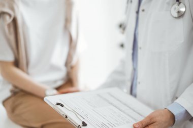 Doktor ve hasta sağlık muayenesi sonuçlarını tartışıyor. Dostane bir doktor, genç bir bayana bir yandan güvence verirken diğer yandan da tıbbi evraklarla pano tutuyor. Tıp konsepti.