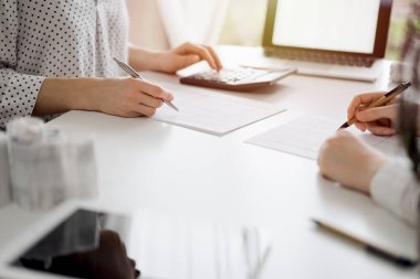 Two accountants using a calculator and laptop computer for counting taxes or revenue balance while rolls of receipts are waiting to be calculating. Business audit and taxes concepts. clipart