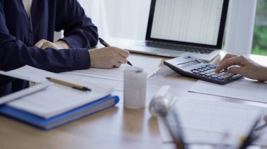Muhasebeciler ya da denetçiler, ofisteki ahşap masada karşılıklı otururken finansal belgeleri gözden geçiriyorlar. Denetim ve vergiler.