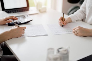 Hesap makinesi ve dizüstü bilgisayar kullanan iki muhasebeci vergileri ve gelir dengesini hesaplamak için beklerken makbuzlar da hesaplanmayı bekliyor. İş denetimi ve vergi kavramları.