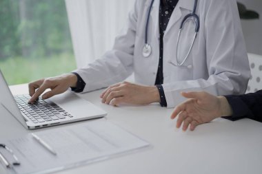 Doktor ve bir hasta klinikte otururken sağlığı tartışıyorlar. Kadın hekim dizüstü bilgisayar kullanıyor. Tıp ve Bilim.