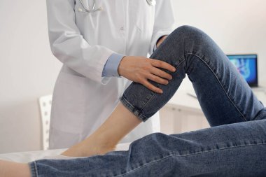 Doktor ve hasta klinikteki sağlık kontrolündeler. Ortopedik genç bir kadının dizini muayene eder. Tıp konsepti.