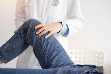 Doktor ve hasta klinikteki sağlık kontrolündeler. Ortopedik genç bir kadının dizini muayene eder. Tıp konsepti.