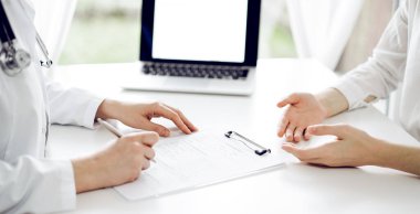 Doktor ve hasta klinikteki beyaz masada yan yana oturuyorlar. Kadın hekim bir kayıt formunu doldururken dinliyor. Tıp konsepti.