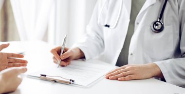 Doktor ve hasta klinikteki beyaz masada oturup bir şeyler tartışıyorlar. Kadın hekim bir kayıt formunu doldururken dinliyor. Tıp konsepti.
