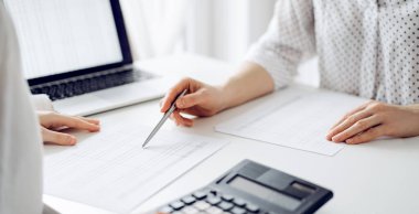 Ofisteki bir müşteriyle ya da meslektaşıyla vergi saymak için hesap makinesi ve dizüstü bilgisayar kullanan bir muhasebeci. İş denetimi ve finans alanında takım çalışması.