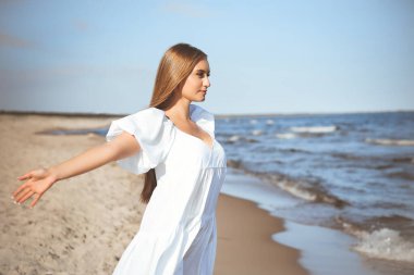 Mutlu gülümseyen güzel kadın okyanus sahilinde beyaz bir yaz elbisesi içinde, kolları açık..