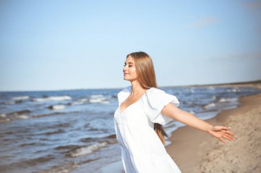Mutlu gülümseyen güzel kadın okyanus sahilinde beyaz bir yaz elbisesi içinde, kolları açık..