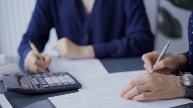 Ofisteki mali belgeleri inceleyen tanınmamış iki muhasebeci ya da denetçi. Denetim ve vergiler.