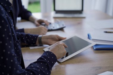 Muhasebeciler ya da denetçiler ofisteki ahşap masada otururken mali belgeleri gözden geçiriyorlar. Profesyoneller tablet bilgisayar kullanarak kağıt raporlarını inceliyor, kapat. Denetim ve vergiler.