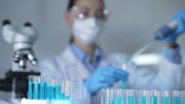 Laboratuvar tüpleri odaklandı, yakın görüş. Kadın araştırmacı, arka planda bir mikro pipet kullanıyor. Tıp ve Bilim.