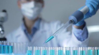 Laboratuvar ortamında test tüplerini mavi bir sıvıyla doldurmak için mikropipetle çalışan kadın bir araştırmacı elin yakın çekimi. Tıp ve bilim konsepti.