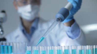 Laboratuvar ortamında test tüplerini mavi sıvıyla doldurmak için mikropipet kullanan kadın araştırmacı. Yakın çekim. Tıp ve Bilim.