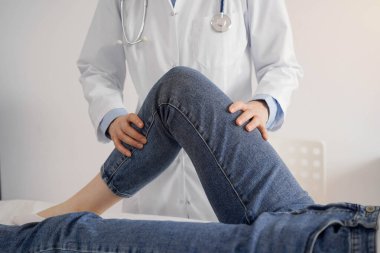 Doktor ve hasta klinikteki sağlık kontrolündeler. Ortopedik genç bir kadının dizini muayene eder. Tıp konsepti.