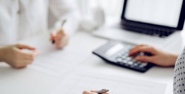 Two accountants using a calculator and laptop computer for counting taxes at white desk in office. Teamwork in business audit and finance. clipart