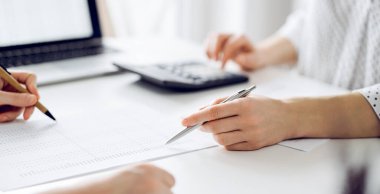 Ofisteki beyaz masada vergileri saymak için dizüstü bilgisayar ve hesap makinesi kullanan iki muhasebeci. İş denetimi ve finans alanında takım çalışması.