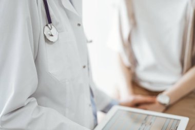 Doktor ve hasta sağlık muayenesi sonuçlarını tartışıyor. Dost canlısı bir doktor bir elinde tablet bilgisayar tutarken diğer elinde genç bir bayana güven veriyor. Tıp konsepti.