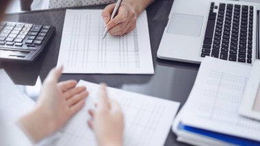 Kadın muhasebeci, hesap makinesi ve dizüstü bilgisayar kullanarak bir müşteriyle ya da meslektaşıyla vergileri sayıp tartışıyor. İş denetleme ekibi.