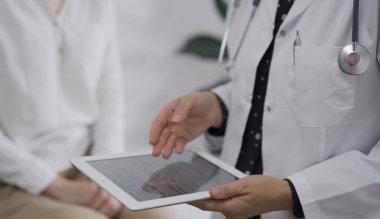 Doktor ve bir hasta. Kadın hekim klinikteki muayene sırasında genç bir kadın dışında tablet bilgisayara işaret ediyor. Tıp konsepti.