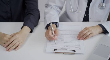 Doktor ve bir hasta klinikteki beyaz masada oturuyorlar. Kadın hekim muayene sırasında not almak için pano kullanıyor. Kapatın. Tıp konsepti.