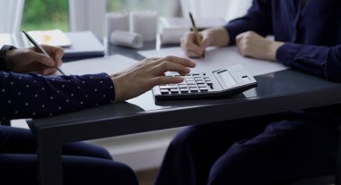 Two unrecognizable accountants or auditors sitting near each other is reviewing financial data in office. Professionals analyzing paper reports and using calculator, view above. Audit and taxes. clipart