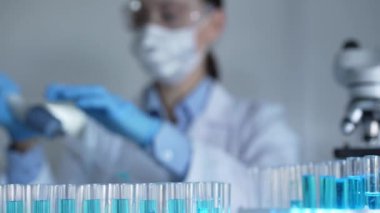 Laboratuvar tüpleri odaklandı, yakın görüş. Kadın araştırmacı, arka planda bir mikro pipet kullanıyor. Tıp ve Bilim.