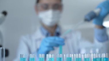 Laboratuvar tüpleri odaklandı, yakın görüş. Kadın araştırmacı, arka planda bir mikro pipet kullanıyor. Tıp ve bilim konsepti.