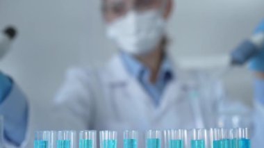Laboratuvar tüpleri odaklandı, yakın görüş. Kadın araştırmacı, arka planda bir mikro pipet kullanıyor. Tıp ve bilim konsepti.