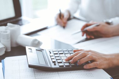 İki muhasebeci vergi veya gelir dengesi saymak için bir hesap makinesi ve dizüstü bilgisayar kullanıyor. İş, denetim ve vergi kavramları.