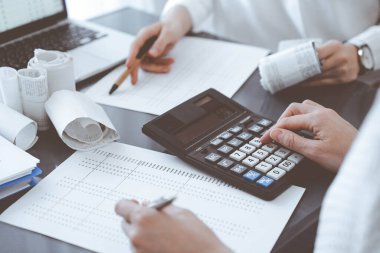 İki muhasebeci vergi veya gelir dengesi saymak için bir hesap makinesi ve dizüstü bilgisayar kullanıyor. İş, denetim ve vergi kavramları.