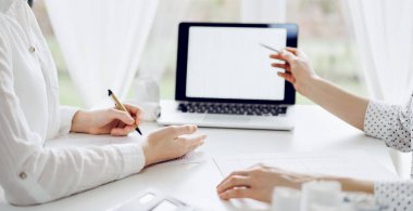 Beyaz masadaki vergileri saymak için dizüstü bilgisayar kullanan iki muhasebeci. İş kadını elinde kalemle ekranı işaret ediyor. İş denetimi ve finans alanında takım çalışması.