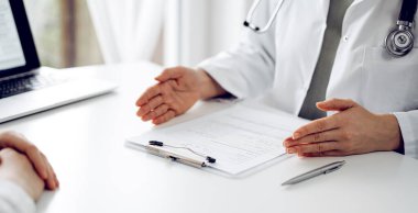Doktor ve hasta klinikteki beyaz masada oturup bir şeyler tartışıyorlar. Kadın hekim bir kayıt formunu doldururken dinliyor. Tıp konsepti.