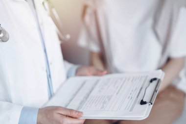Doktor ve hasta mükemmel sağlık muayenesi sonuçlarını tartışıyor. Dost canlısı bir doktor, elinde dosyayla genç bir kadının yanında tıbbi evraklar tutuyor. Tıp konsepti.