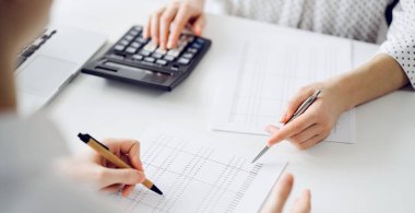 Ofisteki bir müşteriyle ya da meslektaşıyla vergi saymak için hesap makinesi ve dizüstü bilgisayar kullanan bir muhasebeci. İş denetimi ve finans alanında takım çalışması.