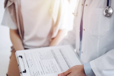 Doktor ve hasta mükemmel sağlık muayenesi sonuçlarını tartışıyor. Dost canlısı bir doktor, elinde dosyayla genç bir kadının yanında tıbbi evraklar tutuyor. Tıp konsepti.