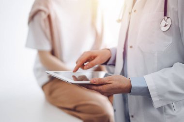 Doctor and patient in clinic. Friendly physician using tablet computer near a young woman. Medicine concept. clipart