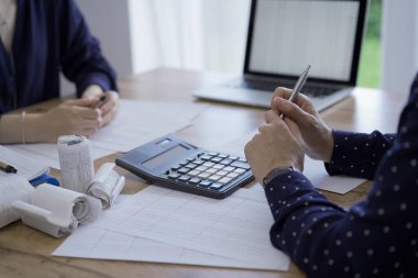 Accountants or auditors reviewing financial documents while using laptop, calculator and sitting opposite one another at the wooden desk in office. Audit and taxes. clipart