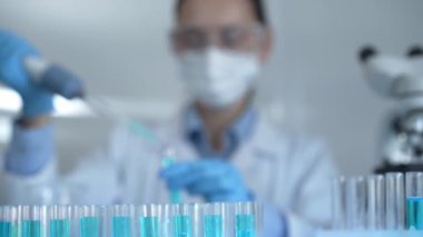 Laboratuvar tüpleri odaklandı, yakın görüş. Kadın araştırmacı, arka planda bir mikro pipet kullanıyor. Tıp ve bilim konsepti.