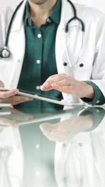 Modern sağlık ortamında dijital tablet kullanan yeşil gömlekli bir doktor hasta verileriyle etkileşime geçiyor. Tıp konsepti.