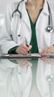 Kadın doktor, pano kullanıyor ve tıbbi bir ofisteki cam masaya notlar alıyor, dikey açıdan yakından bakıyor. Tıp konsepti.