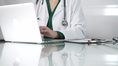Masanın üzerinde steteskop, gözlük ve not panosuyla bilgisayarın klavyesine yazarak teknolojinin sağlık hizmetlerine entegrasyonunu vurgulayan kadın doktorların ellerini kapatın.