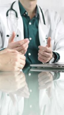 Steteskop ve laboratuvar önlüğü giyen doktor, masadaki bir hastaya dizüstü bilgisayarla teşhis koymayı açıklarken elleriyle işaret ediyor. Tıp konsepti.