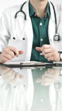 Erkek doktor bir dosya kullanıyor ve bir tıp bürosundaki cam masaya notlar alıyor, dikey açıdan yakından bakıyor. Tıp konsepti.