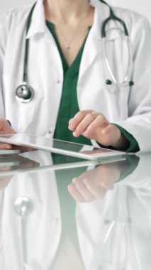 Modern sağlık ortamında dijital tablet kullanan beyaz önlüklü kadın doktor, hasta verileriyle etkileşime geçiyor..