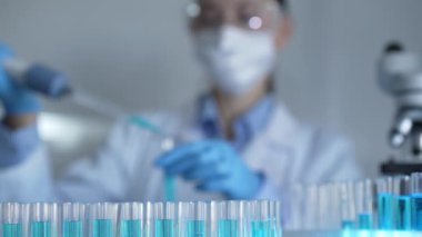 Laboratuvar tüpleri odaklandı, yakın görüş. Kadın araştırmacı, arka planda bir mikro pipet kullanıyor. Tıp ve Bilim.